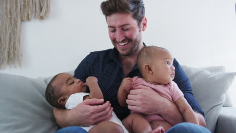 Father-Sitting-On-Sofa-At-Home-Cuddling-Baby-Son-And-Daughter
