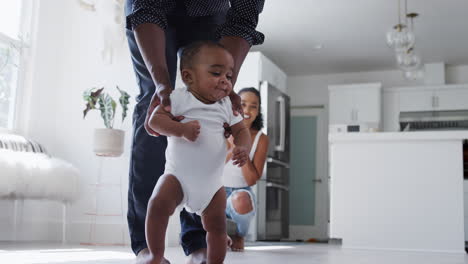 Parents-Encouraging-Smiling-Baby-Son-To-Take-First-Steps-And-Walk-At-Home