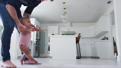 Close-Up-Of-Father-Encouraging-Smiling-Baby-Daughter-To-Take-First-Steps-And-Walk-At-Home
