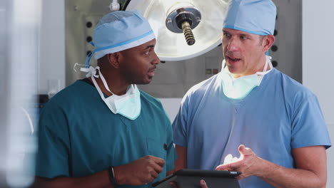Zwei-Männliche-Chirurgen-In-Kitteln-Schauen-Im-Operationssaal-Eines-Krankenhauses-Auf-Ein-Digitales-Tablet