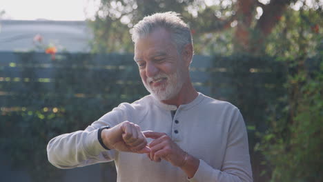 Senior-Hispanic-Man-Checking-Smart-Watch-In-Garden-At-Home
