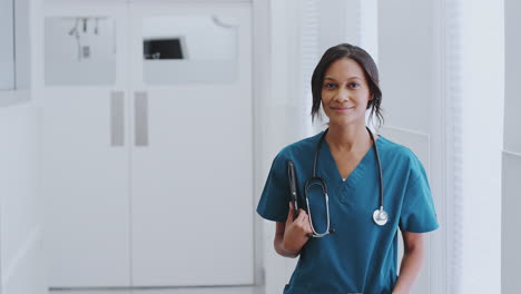 Portrait-Of-Female-Doctor-With-Stethoscope-Wearing-Scrubs-In-Hospital-Corridor-With-Digital-Tablet