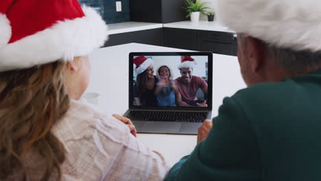 Multi-Generation-Hispanic-Family-Wearing-Santa-Hats-With-Laptop-Having-Video-Chat-At-Christmas
