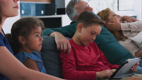 Eine-Hispanische-Familie-Mit-Mehreren-Generationen-Entspannt-Sich-Auf-Dem-Sofa,-Während-Ihr-Enkel-Mit-Einem-Digitalen-Tablet-Spielt