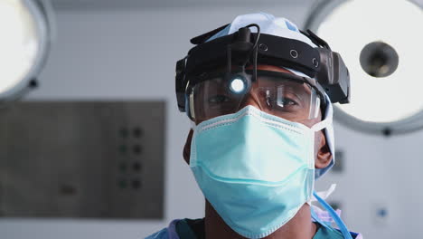 Porträt-Eines-Männlichen-Chirurgen-Mit-Schutzbrille,-Scheinwerfer-Und-Maske-Im-Operationssaal-Des-Krankenhauses