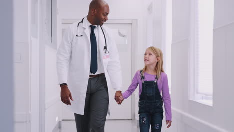 Male-Paediatric-Doctor-Giving-Young-Girl-Patient-High-Five-In-Hospital-Corridor