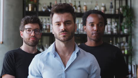 Portrait-Of-Male-Owner-Of-Restaurant-Bar-With-Team-Of-Male-Waiting-Staff-Standing-By-Counter