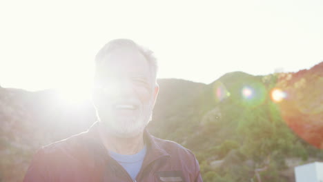 Portrait-Of-Smiling-Hispanic-Senior-Man-Outdoors-In-Countryside-Against-Flaring-Sun