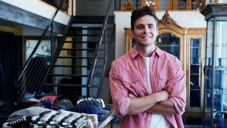 Portrait-Of-Smiling-Male-Owner-Of-Fashion-Store-Standing-In-Front-Of-Clothing-Display