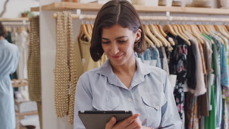 Portrait-Of-Female-Owner-Of-Fashion-Store-Using-Digital-Tablet-To-Check-Stock-In-Clothing-Store