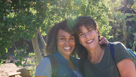 Portrait-Of-Two-Senior-Female-Friends-Hiking-Along-Trail-In-Countryside-Together