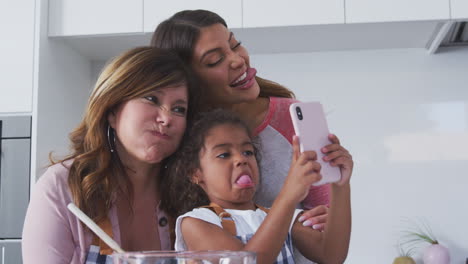 Familia-Femenina-Hispana-Multigeneracional-Tomándose-Selfie-Mientras-Preparan-Pasteles-Juntos-En-La-Cocina
