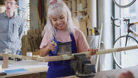 Female-Apprentice-In-Carpentry-Workshop-For-Building-Bicycles-Frame-Sawing-Wood