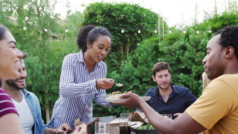 Woman-Serving-Group-Of-Multi-Cultural-Friends-At-Home-At-Table-Enjoying-Food-At-Summer-Garden-Party