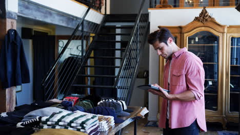 Male-Owner-Of-Fashion-Store-Using-Digital-Tablet-To-Check-Stock-In-Clothing-Store