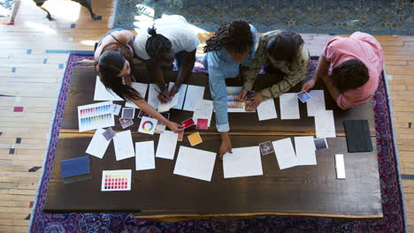 Overhead-View-Of-Team-Having-Creative-Design-Meeting-Around-Wooden-Table-In-Office