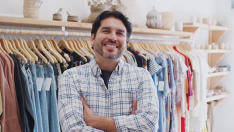 Portrait-Of-Male-Owner-Of-Fashion-Store-Standing-In-Front-Of-Clothing-On-Rails