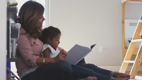 Hispanic-Grandmother-And-Granddaughter-Sitting-On-Floor-Of-Childrens-Bedroom-Reading-Book-Together