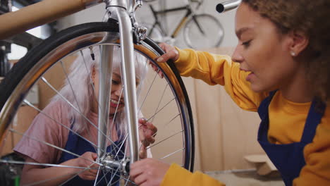 Weibliche-Auszubildende-Prüfen-In-Der-Werkstatt-Das-Rad-Eines-Handgefertigten-Fahrradrahmens