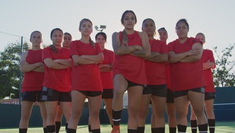 Portrait-Of-Determined-Female-Soccer-Team-With-Ball-On-Training-Ground-Against-Flaring-Sun