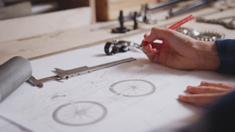 Close-Up-Of-Female-Engineer-In-Workshop-Making-Notes-On-Plan-For-Handmade-Bicycle