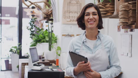 Portrait-Of-Female-Owner-With-Digital-Tablet-Standing-Behind-Sales-Desk-Of-Florists-Store