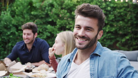 Portrait-Of-Man-With-Friends-At-Home-Sitting-At-Table-Enjoying-Food-At-Summer-Garden-Party