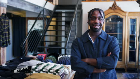 Portrait-Of-Smiling-Male-Owner-Of-Fashion-Store-Standing-In-Front-Of-Clothing-Display