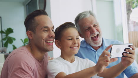 Multi-Generation-Male-Hispanic-Family-On-Sofa-At-Home-Posing-For-Selfie-On-Mobile-Phone