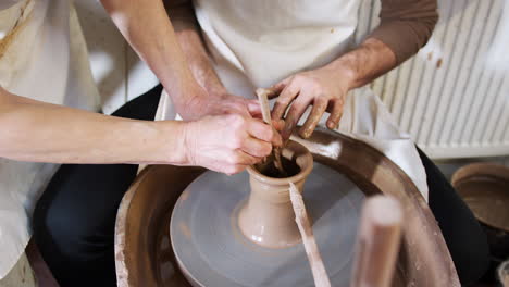 Close-Up-Of-Male-Teacher-Helping-Man-Sitting-At-Wheel-In-Pottery-Class