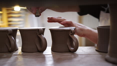 Close-Up-Of-Male-Potter-Putting-Studio-Stamp-Onto-Base-Of-Clay-Mugs