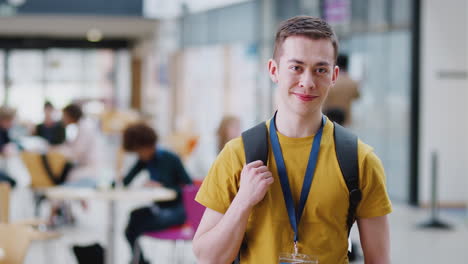 Portrait-Of-Smiling-Male-College-Student-In-Busy-Communal-Campus-Building