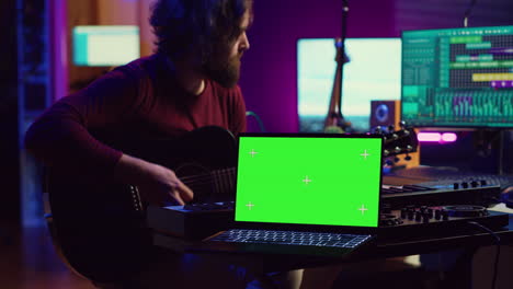 Guitarist-playing-his-acoustic-instrument-next-to-greenscreen-on-laptop