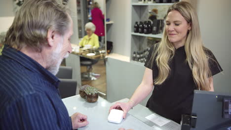 Senior-Man-Making-Contactless-Payment-To-Stylist-In-Salon-With-Credit-Card