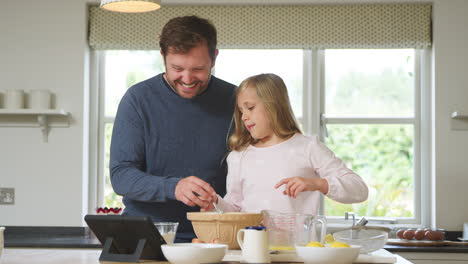 Father-And-Daughter-In-Pyjamas-Baking-In-Kitchen-At-Home-Following-Recipe-On-Digital-Tablet
