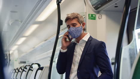 Businessman-Stands-In-Train-Carriage-Talking-On-Mobile-Phone-Wearing-PPE-Face-Masks-During-Pandemic