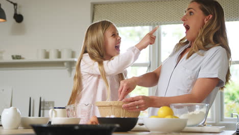 Mother-And-Daughter-Wearing-Pyjamas-Having-Messy-Fun-As-They-Bake-In-Kitchen-At-Home-Together