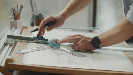 Architect's-desk:-drawings-tape-measure-ruler-and-other-drawing-tools.-Engineer-works-with-drawings-in-a-bright-office-close-up.-Insturments-and-office-for-designer.-Male-hands-draw-with-a-pencil.