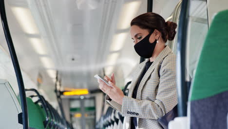 Businesswoman-Stands-In-Train-Carriage-Using-Mobile-Phone-Wearing-PPE-Face-Masks-During-Pandemic