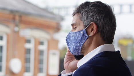 Businessman-On-Railway-Platform-Talking-On-Mobile-Phone-Wearing-PPE-Face-Mask-During-Health-Pandemic