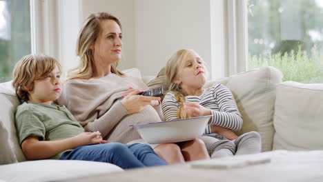 Schwangere-Mutter-Mit-Kindern-Sitzt-Zu-Hause-Auf-Dem-Sofa,-Lacht-Und-Schaut-Mit-Popcorn-Fern