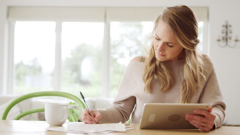 Woman-With-Digital-Tablet-Sitting-At-Table-At-Home-Reviewing-Domestic-Finances