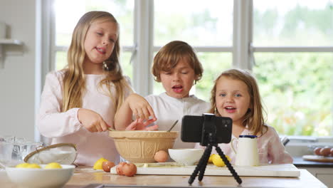 Children-In-Pyjamas-Baking-In-Kitchen-At-Home-Whilst-Vlogging-On-Mobile-Phone