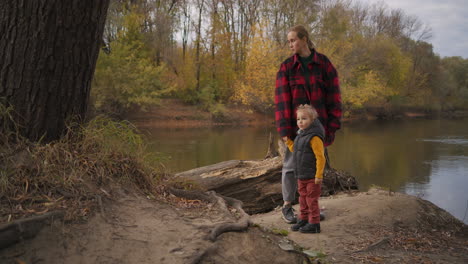 single-mother-is-walking-with-little-son-at-nature-resting-at-woodland-walking-together-at-autumn-day-viewing-small-river-in-forest