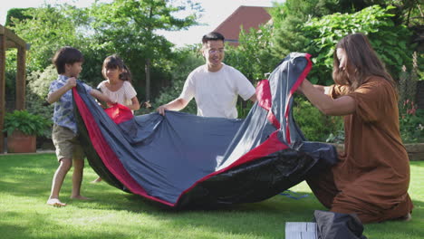 Asian-Family-Having-Fun-In-Garden-At-Home-Putting-Up-Tent-For-Summer-Camping-Trip-Together