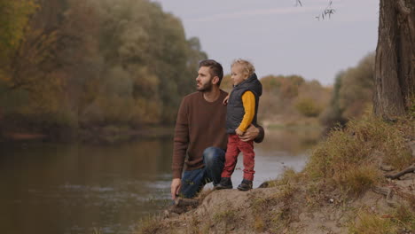 joyful-child-is-standing-near-father-on-shore-of-river-in-autumn-forest-happy-family-relationships-spending-weekend-together-resting-at-nature