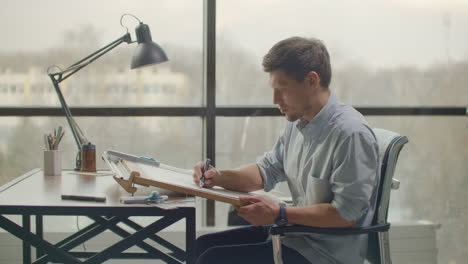 Architect-man-sits-at-drafting-table-in-modern-industrial-office-during-the-day.-Architect-working-on-blueprint-with-spesial-tools-and-pencil-close-up.-Male-architect-at-work-only-hands-with-ruler-and-pencil.-Design-of-the-house.-Engineer.-Tools-for-drawing.-Creating-a-drawing.