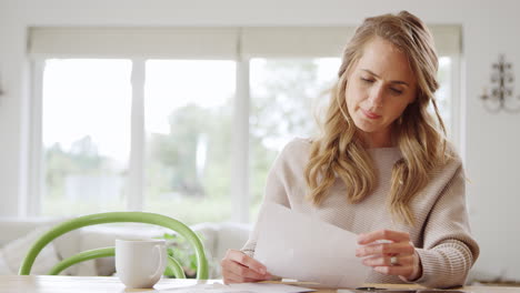Worried-Woman-Sitting-At-Table-At-Home-Reviewing-Domestic-Finances-Opening-Letter-With-Bill