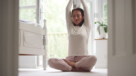 Reife-Asiatische-Frau-Im-Schlafanzug-Sitzt-Auf-Dem-Boden-Des-Schlafzimmers-Und-Meditiert-In-Yoga-Pose-–-Aufgenommen-In-Zeitlupe
