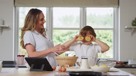 Mother-And-Son-In-Pyjamas-Making-Funny-Faces-With-Lemons-As-They-Bake-In-Kitchen-At-Home-Together